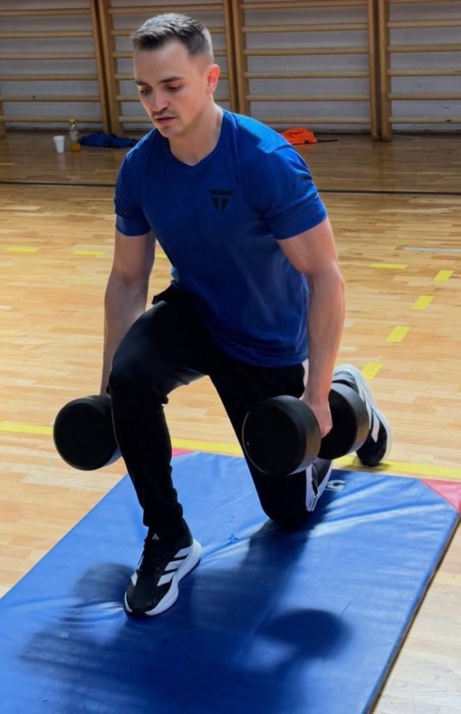 Një pjesëmarrës duke bërë ushtrime me pesha dore në sallën sportive.